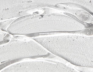 Primissimo piano di gel trasparente su una superficie bianca, con fossette e riflessi che creano un bagliore elegante.