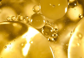 Gocce di olio e bolle in primo piano su uno sfondo dorato e luminoso, creando un effetto dinamico e astratto.