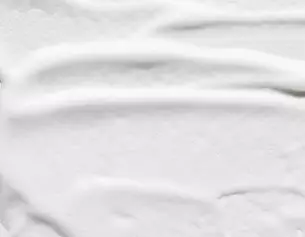 Superficie liscia di crema bianca con leggere striature, riflettendo luminosita e texture setosa.