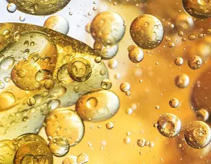 Bollicine e gocce d&apo;olio fluttuano in una soluzione dorata, creando un affascinante gioco di luce e texture.