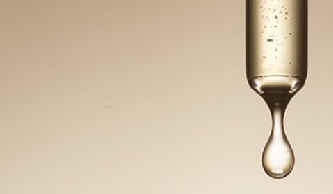 Three glass pipettes with liquid inside, suspended above a soft, beige background, with drops of liquid forming at the tips.