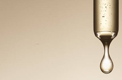 Three glass pipettes with liquid inside, suspended above a soft, beige background, with drops of liquid forming at the tips.