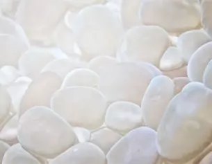 Moltitudini di ciottoli bianchi lucidi che si riflettono alla luce, creando un effetto organico e sereno.