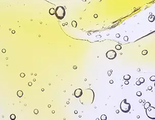 Bollicine e gocce di un liquido trasparente di colore giallo, sfondo chiaro che crea un effetto luminoso e vibrante.