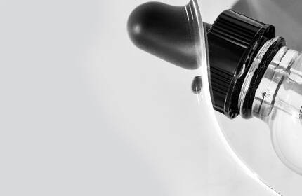Close-up of a white machine with a black control knob and a transparent component, set against a light gray background.