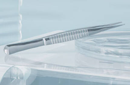 A close-up of a minimalist surgical or dental setting featuring a sleek, metallic tweezer resting on a clear surface, with soft lighting creating a calm atmosphere.