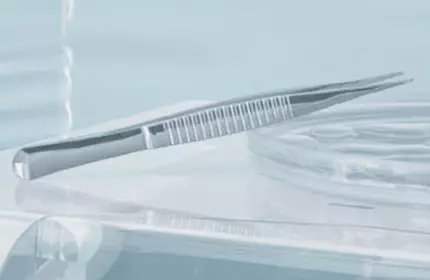 A close-up of a minimalist surgical or dental setting featuring a sleek, metallic tweezer resting on a clear surface, with soft lighting creating a calm atmosphere.