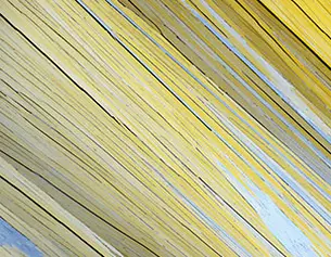 Close-up of long, thin yellow and gray wooden planks arranged diagonally, creating a textured and colorful pattern.