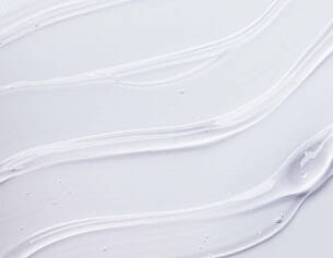 A smooth, white cream or gel smeared on a light background, with flowing textures and glossy highlights.