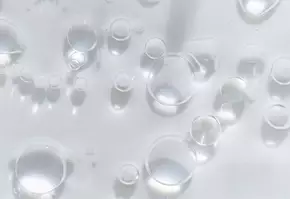 Gocce d'acqua trasparenti su uno sfondo bianco, creando un effetto di luce e riflessione.