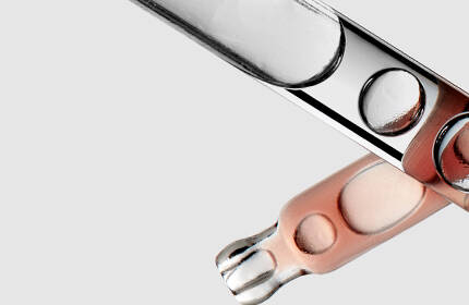 Close-up of glass test tubes with a pink liquid inside, arranged against a light background.