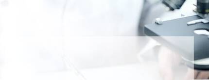 Un laboratorio scientifico con un microscopio e un ricercatore che sta aggiungendo un liquido a una piastra di petri.