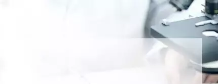 Un laboratorio scientifico con un microscopio e un ricercatore che sta aggiungendo un liquido a una piastra di petri.