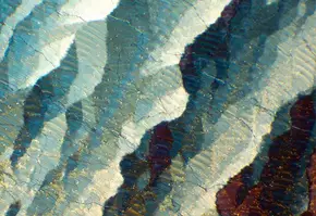 Dettaglio di una superficie minerale con striature di blu, bianco e marrone, creando un effetto di luce e trasparenza.
