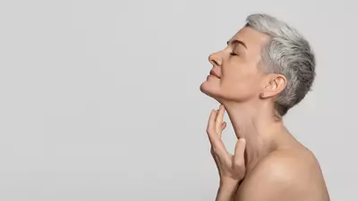 Una donna con capelli corti e grigi, in posa profilo, si tocca delicatamente il mento con una mano, mostrando una serena espressione.
