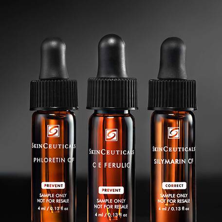 Una bottiglia di vetro ambrato di SkinCeuticals Silymarin CF, tra altre due bottiglie simili CE Ferulic e Phloretin CF, su sfondo scuro.