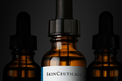 Tre flaconi contagocce ambrati, quello centrale con etichetta "SkinCeuticals", su sfondo scuro