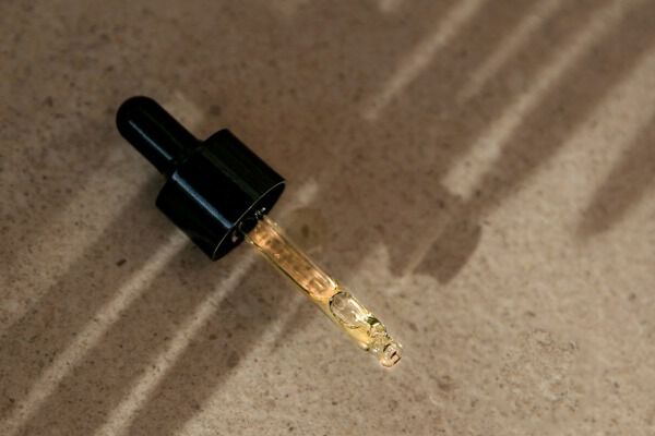 Un primo piano di un contagocce riempito con un liquido dorato, che proietta ombre su una superficie chiara.