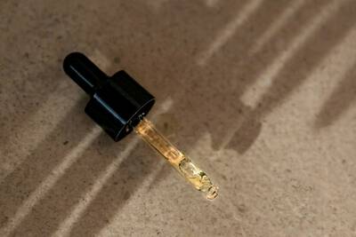 Un primo piano di un contagocce riempito con un liquido dorato, che proietta ombre su una superficie chiara.