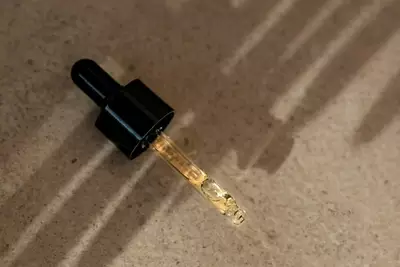 Un primo piano di un contagocce riempito con un liquido dorato, che proietta ombre su una superficie chiara.