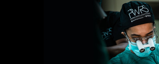 Un chirurgo indossa una mascherina e occhiali ingranditori, concentrato durante un intervento chirurgico.