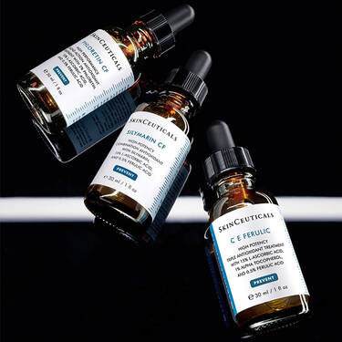 Una bottiglia di vetro ambrato di SkinCeuticals Silymarin CF, posizionata tra altre due bottiglie simili, C E Ferulic e Phloretin CF, il tutto su uno sfondo scuro​
