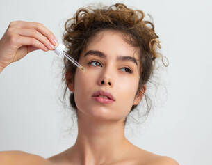 Una giovane donna applica un siero sul viso, mostrando una pelle luminosa e curata.