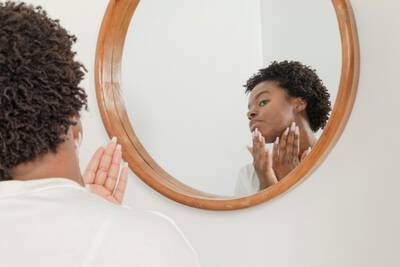 Una donna che applica prodotti per la cura della pelle davanti a uno specchio.